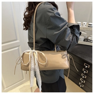 Detail of beige baguette bag featuring a white lace bow and side drawstring details