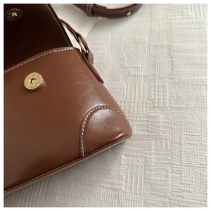 Close-up of brown leather bag showing magnetic closure and reinforced stitching detail