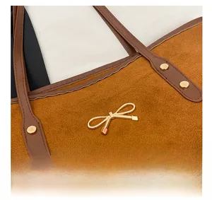 Close-up of brown suede tote bag with golden bow hardware and leather shoulder strap