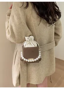 Detail of vintage coffee bucket bag with pearl handle and chain worn over beige coat