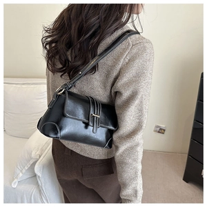 Detail of black leather underarm bag with decorative buckle shown on shoulder