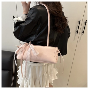 Detail of pink glossy shoulder bag featuring a white lace ribbon bow on the side