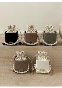Multiple colors of corduroy bucket bags with pearl handles and metal chains on stone steps