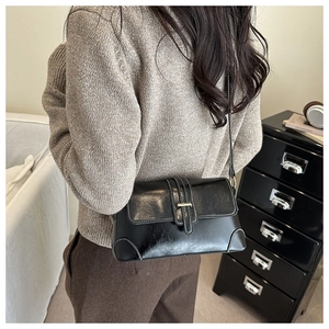 Detail of black leather crossbody bag with white contrast stitching and metal buckle