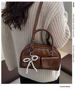 Detail view of dark brown Boston bag with elegant white pearl bow pendant charm