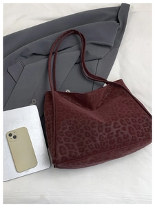 Detail of dark red leopard print tote bag placed on white fabric with modern lifestyle props