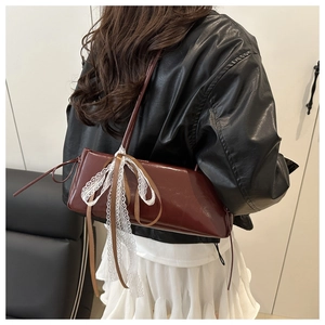Close-up of the red-brown glossy leather baguette bag with white lace bow and strap details