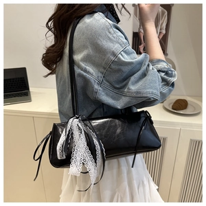 Detail of black patent leather underarm bag featuring white lace trim and ribbon bow