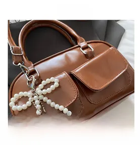 Detail of brown leather bowling bag showing front pockets and pearl bow pendant
