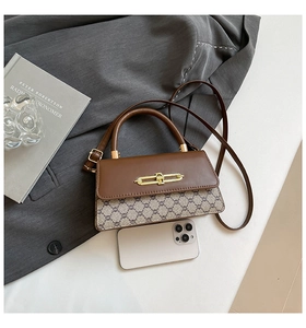 Close-up of retro crossbody bag with monogram texture and golden buckle next to a phone