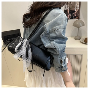 Glossy black baguette bag with white lace bow detail shown in a modern lifestyle setting