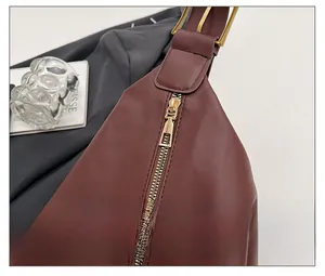 Detail shot of smooth golden zipper closure on dark red leather shoulder bag