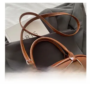 Detail of adjustable shoulder strap and metal buckle on brown faux leather handbag