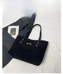 Close-up of black suede tote bag featuring a gold bow detail and twin handles