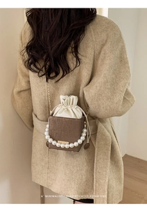 Rear view of brown drawstring bucket bag with pearl handle on model in wool coat