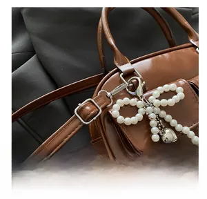 Detail view of adjustable strap buckle and pearl bow charm on brown leather handbag