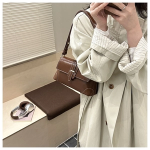 Detail showing deep brown faux leather shoulder bag worn over a beige trench coat