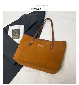 Detail of a brown suede tote bag with a golden bow hardware and rivet leather handles