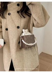 Brown box shoulder bag with pearl handle and silk drawstring on a beige wool coat