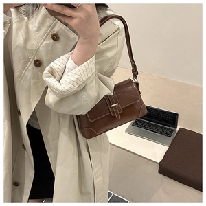 Detail of vintage brown shoulder bag with white stitching and gold buckle on a model