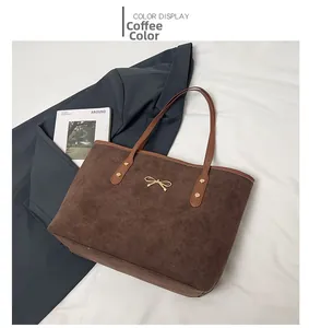 Detail of a brown faux suede tote bag featuring a golden bow metal buckle on a white cloth