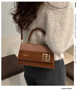 Detailed close-up of brown textured leather crossbody bag with golden hardware and logo
