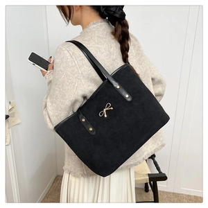 Detail of black suede tote bag featuring a gold bow accent and leather strap on model