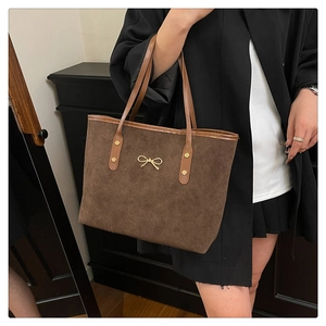 Close-up of brown suede tote bag featuring gold bow hardware and reinforced rivets