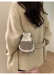 Detail of vintage velvet box bag with pearl handle and golden chain on beige coat
