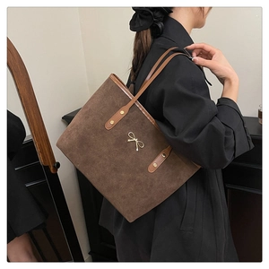 Detail of dark brown suede tote bag with golden bow ornament on model's shoulder