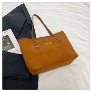 Detail view of suede tote bag with golden bow ornament and dark brown leather strap