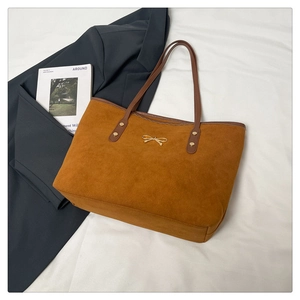 Detailed view of caramel suede tote bag with brown leather handles and gold bow accent