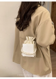 Detail of white bucket bag featuring a large pearl handle and fine gold chain strap