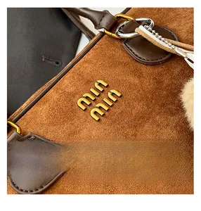 Detail der Boston-Tasche aus braunem Wildleder mit Goldlogo und weichem Plüsch-Anhänger