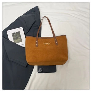 Close-up of caramel suede tote bag with gold bow detail and smartphone for size reference