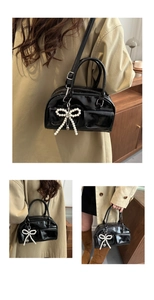 Detail of black patent leather baguette bag with pearl bow charm and glossy finish