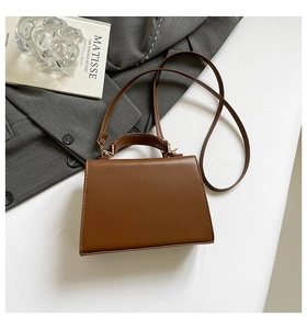 Chic brown trapezoid handbag with gold hardware and top handle in a lifestyle setting