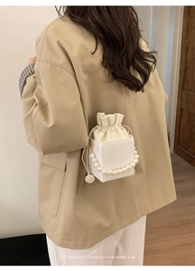 Detail of white bucket bag featuring large pearl handle and cream drawstring lining