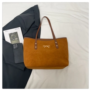 Detail of a brown tote bag featuring a gold bow logo and stylish rivet accents