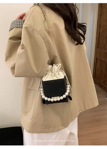 Minimalist bucket bag detail with pearl handle and chain strap on khaki coat