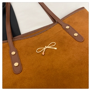 Detailed macro view of the brown suede tote bag featuring a gold bow metallic buckle