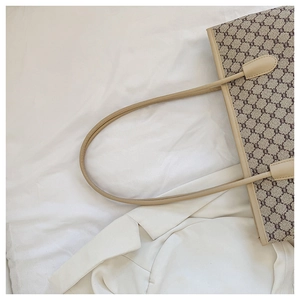 Detail of monogram tote bag with leather straps on white textured clothing