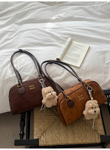 Detail von Boston-Taschen aus Wildleder in Braun und Karamell mit goldenem Logo und Anhänger