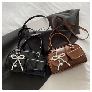 Detail of Boston bags with glossy finish, pearl bows and heart charms in black and brown