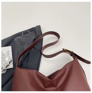 Detail of burgundy leather tote bag with gold buckle on a stylish office setting