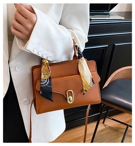 Detail of a brown leather handbag with a silk scarf handle and golden oval metal clasp