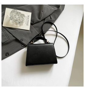 Minimalist black trapezoid handbag with a matching slim shoulder strap and golden hardware