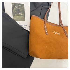 Close-up of brown suede tote bag featuring a gold metal bow and smooth PU leather strap