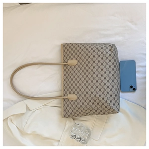 Detail of large tote bag with repetitive pattern and leather handle next to a smartphone