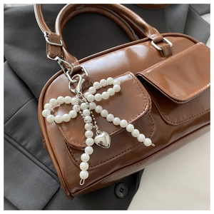 Detail of brown glossy leather handbag with pearl bow charm and silver heart pendant